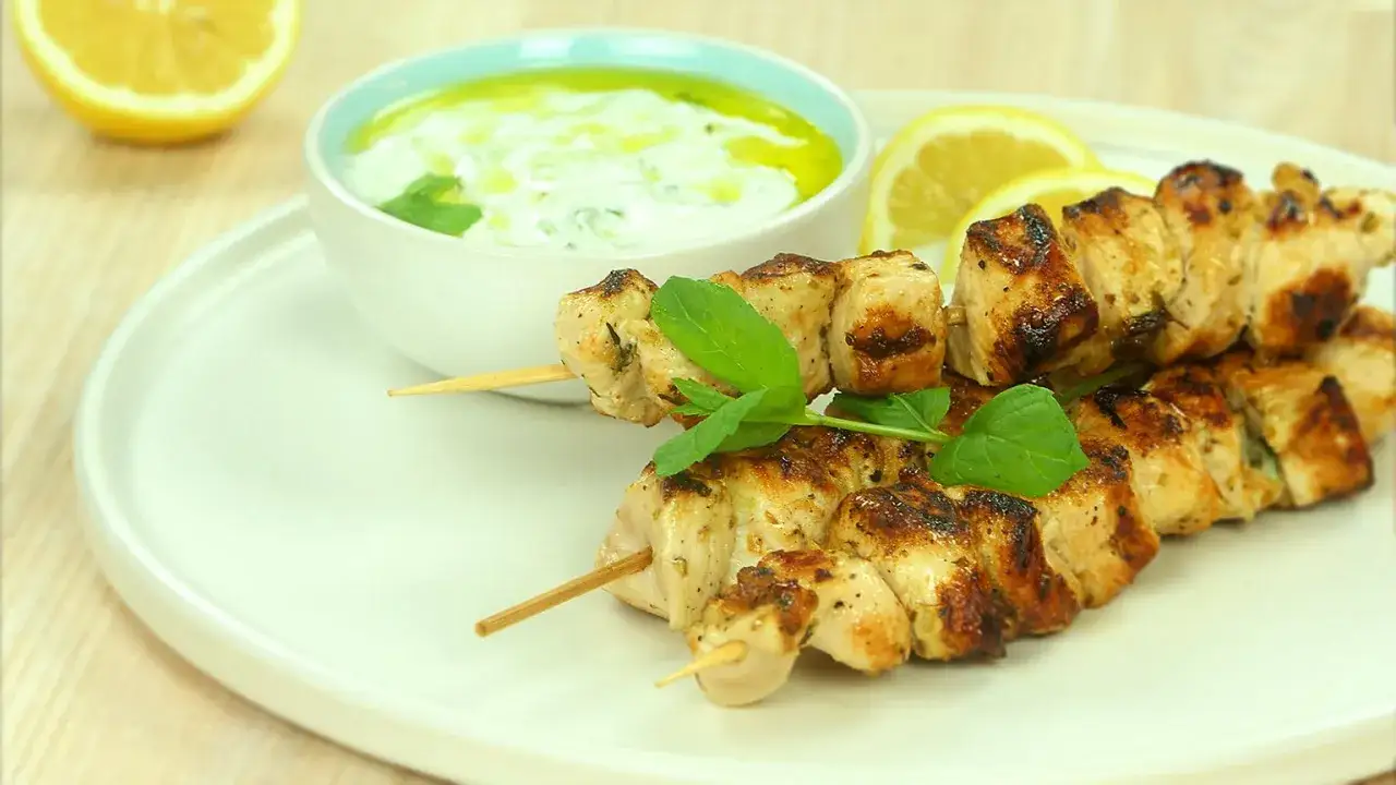Pyszne souvlaki z kurczaka na patyczkach, podane z sosem tzatziki, cytryną i świeżą miętą.