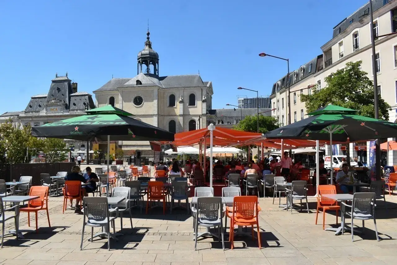 Terrasse animée d'un restaurant le Mans, sous des parasols verts et orange, avec des clients attablés profitant du soleil.