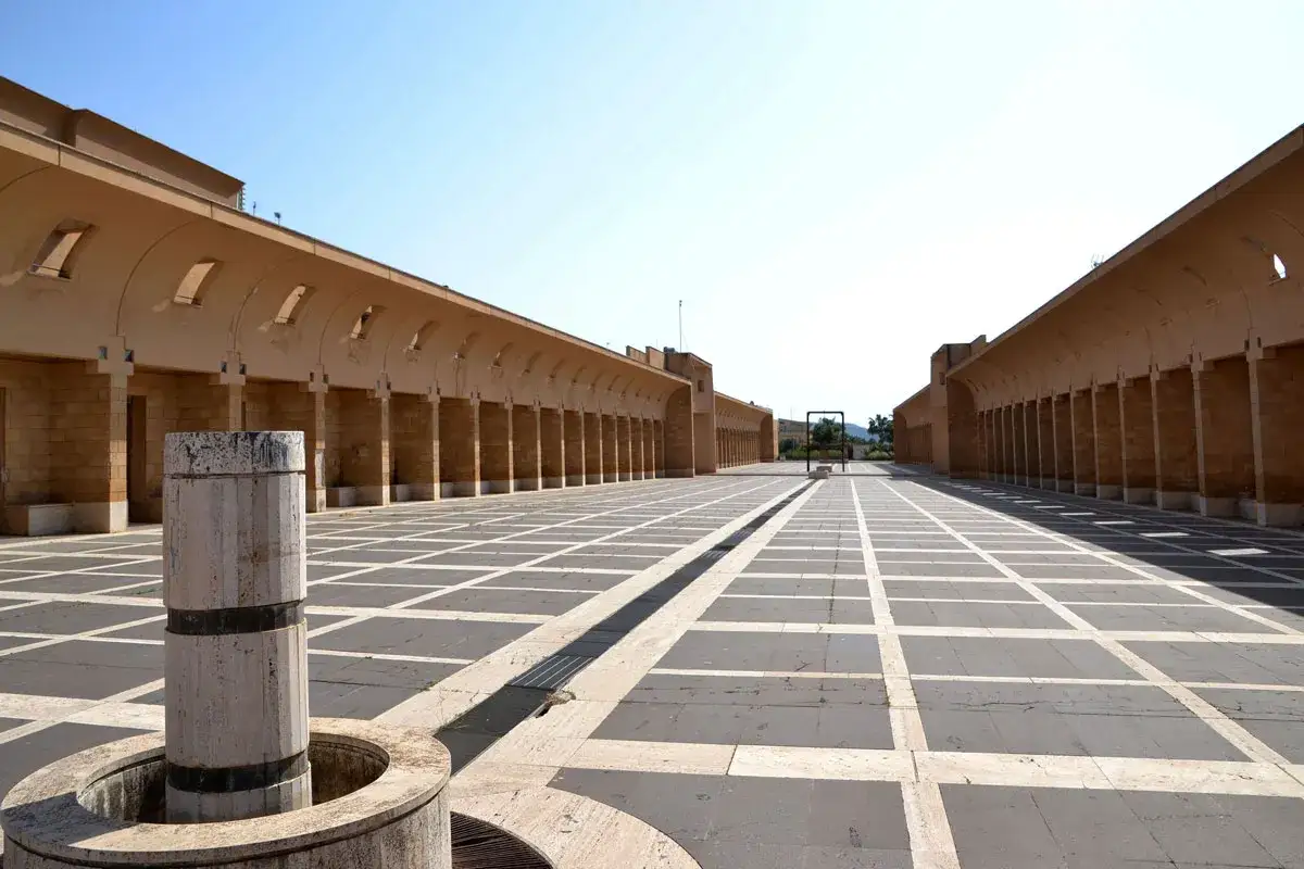 Piazza con portici e pavimentazione a scacchi, un monumento circolare in primo piano. Alberto Selvestrel potrebbe aver ammirato questo luogo.