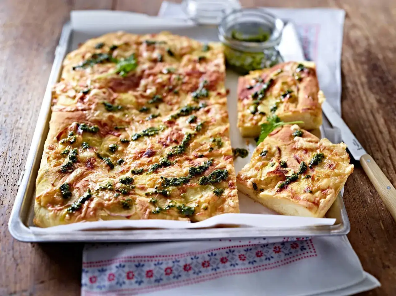 Ein rustikaler Kartoffelkuchen nach altem Rezept, belegt mit Käse und Kräutern, serviert auf einem Blech.