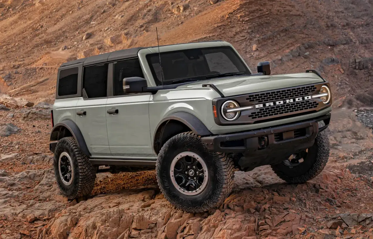 Zielony Ford Bronco z czarnym dachem pokonuje skalisty teren.