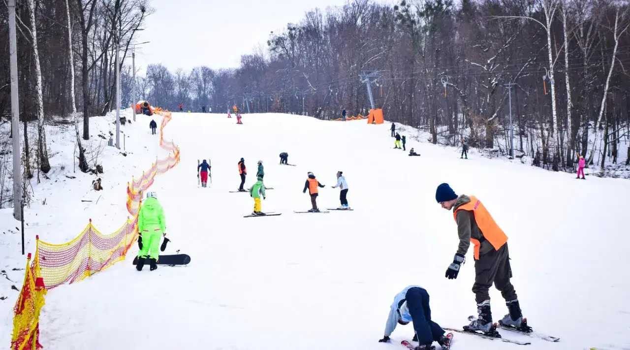 Bambini e adulti sciano e fanno snowboard sui **impianti sciistici del centro Italia**. Un istruttore con pettorina arancione guida gli allievi.