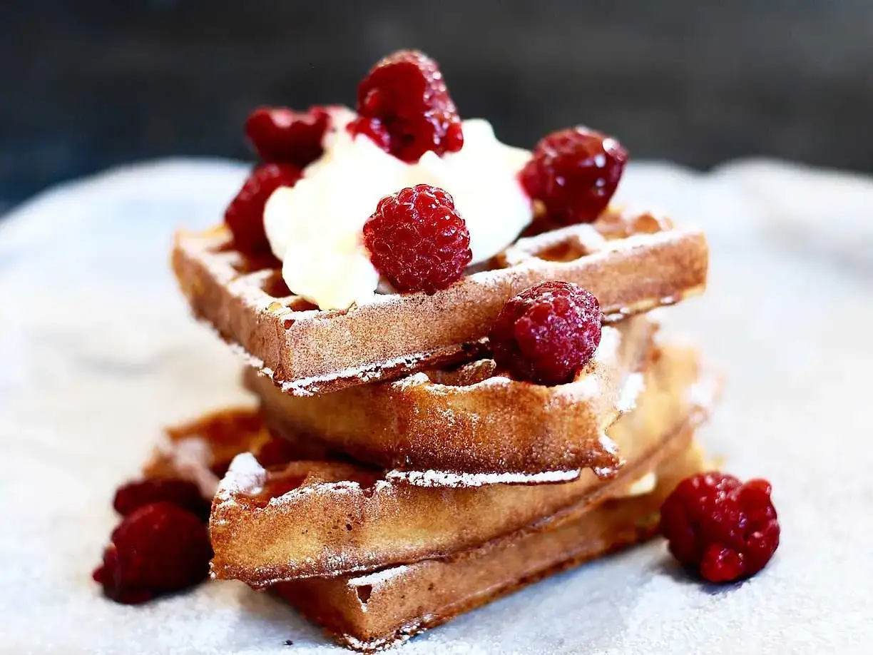 En stapel belgiska våfflor toppade med vispgrädde och färska hallon, pudrade med florsocker. En härlig frukost eller dessert!