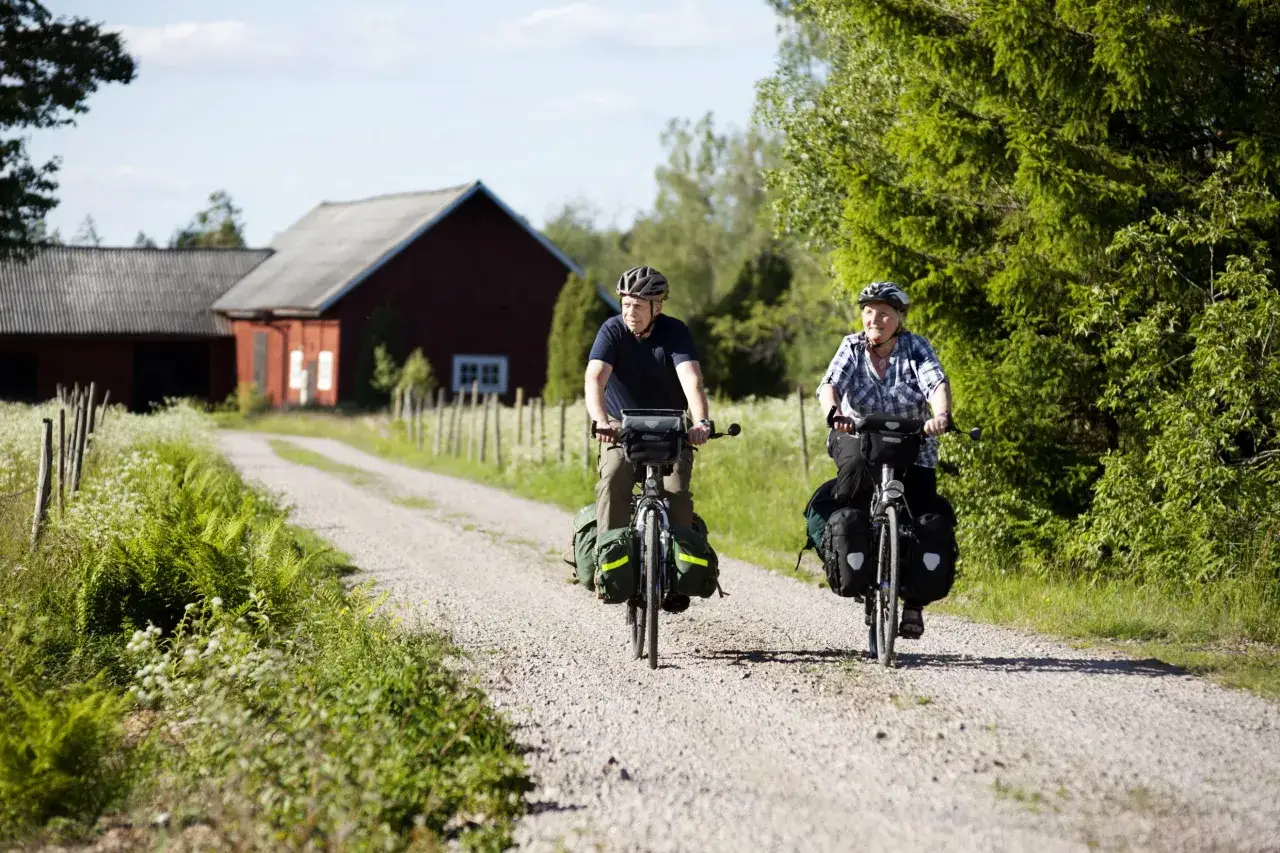 Two cyclists enjoy a scenic gravel road, a perfect setting for Sweden bike tours, with a red barn in the background.