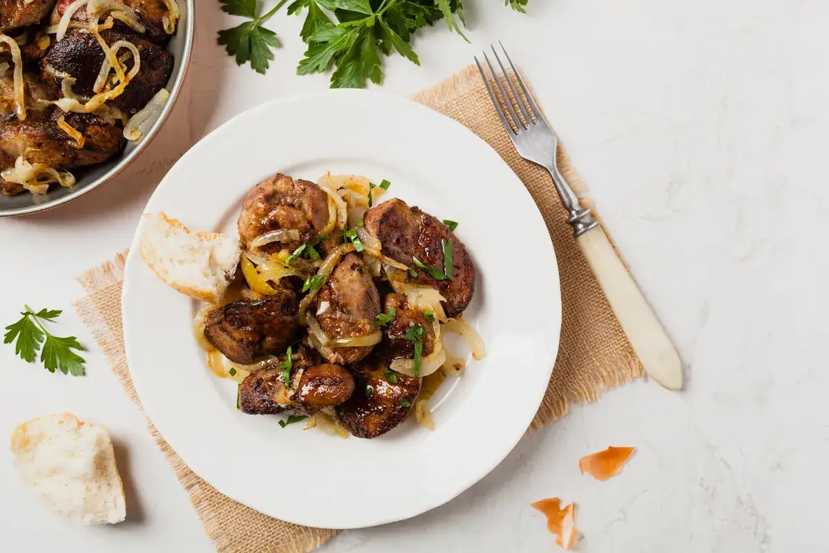 Piatto di fegatini di pollo saltati con cipolle, guarniti con prezzemolo fresco e accompagnati da pane.