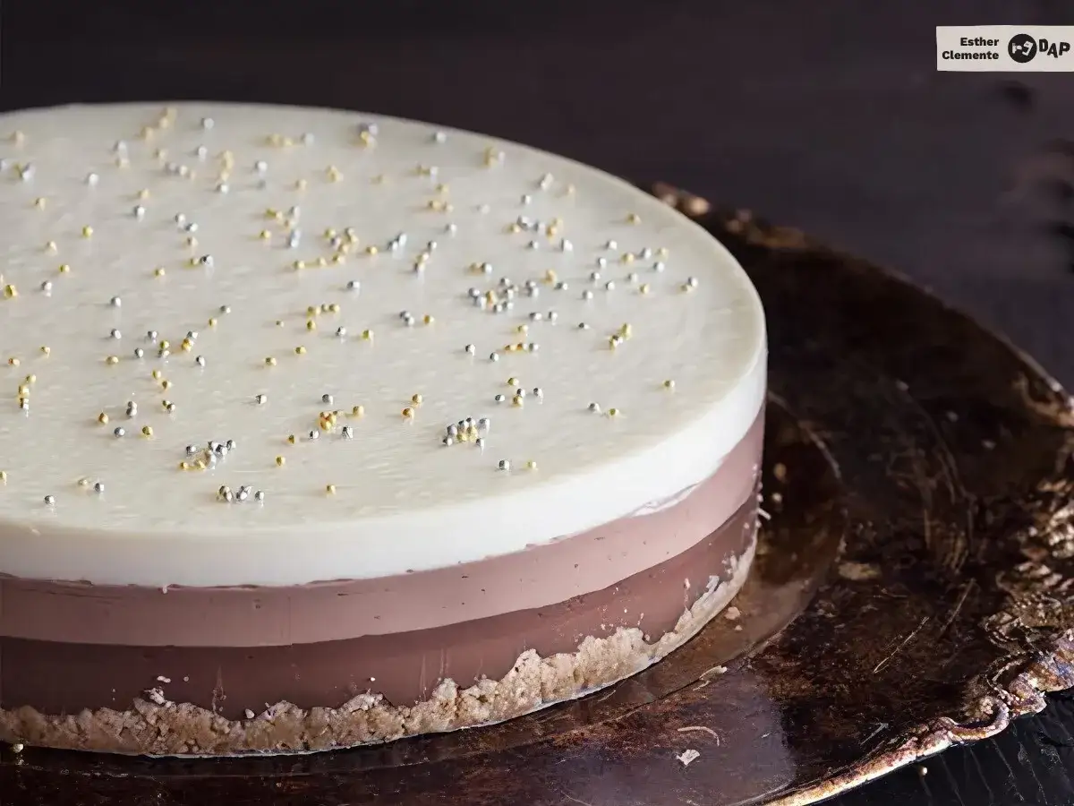 Tarta tres chocolates, con capas de chocolate blanco, con leche y negro, decorada con perlitas doradas y plateadas sobre una base crujiente.
