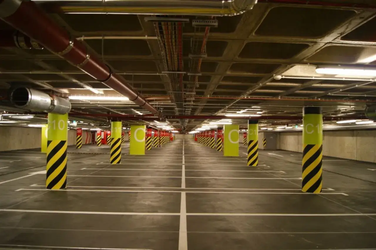 Wrocław Główny parking cennik: Puste, oświetlone wnętrze podziemnego parkingu z rzędami żółto-czarnych słupów i białymi liniami wyznaczającymi miejsca.