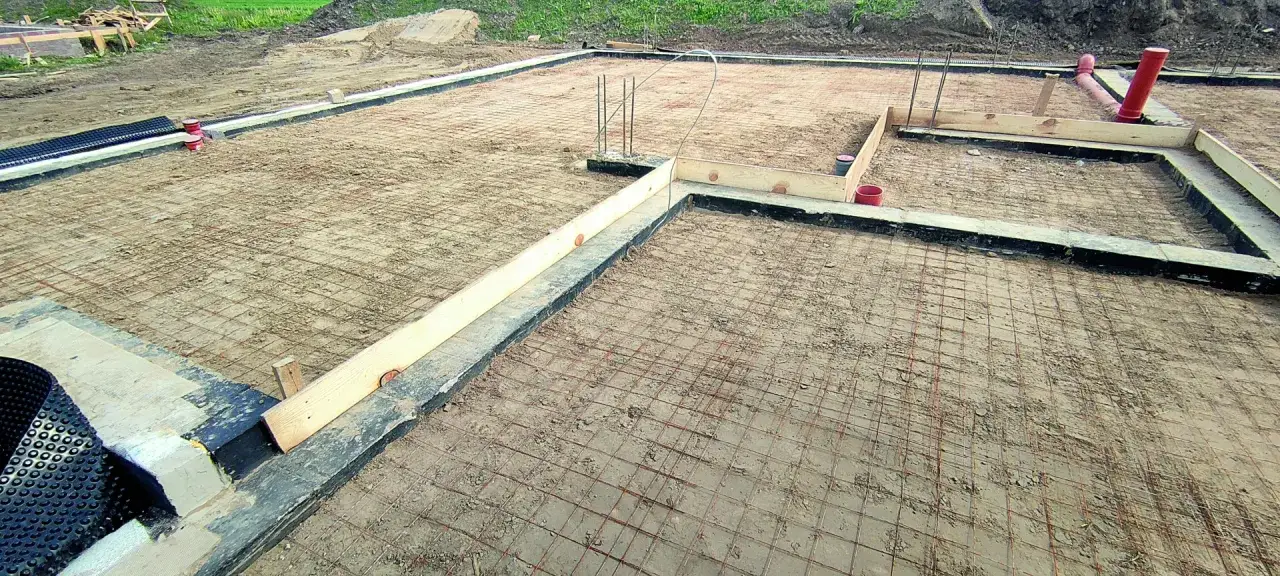 Fundament pod budowę z siatką zbrojeniową i szalunkiem. Widać rury kanalizacyjne i elementy izolacji. Minimalna grubość chudziaka jest kluczowa.