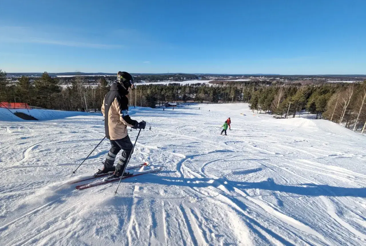En person åker skidor i Luleå en solig dag. Barn åker skidor i bakgrunden.