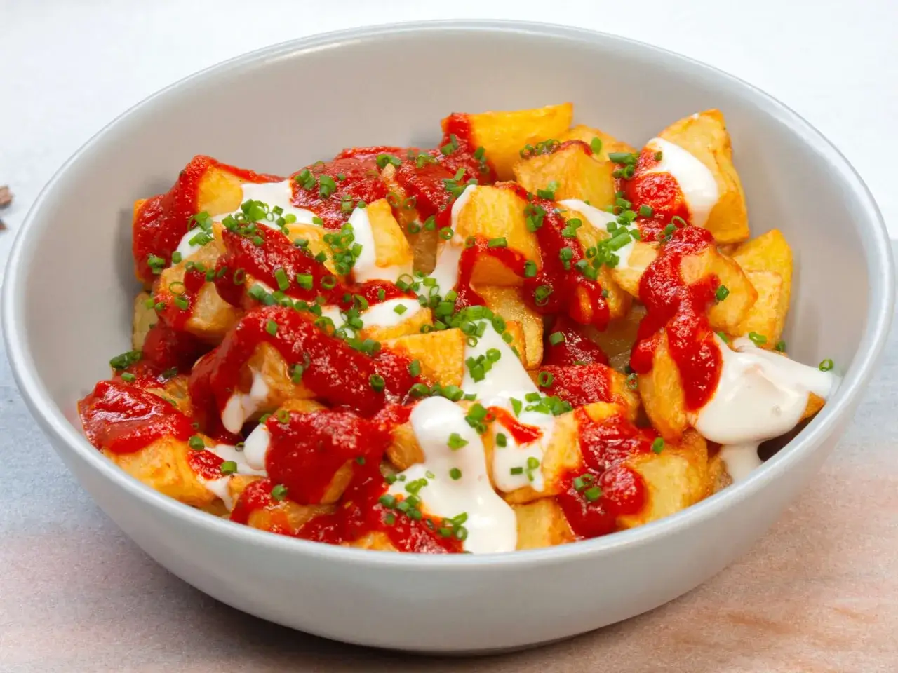Knusprige Kartoffelwürfel, übergossen mit scharfer Tomatensauce und cremiger Aioli, bestreut mit Schnittlauch. Ein Klassiker: Patatas bravas!