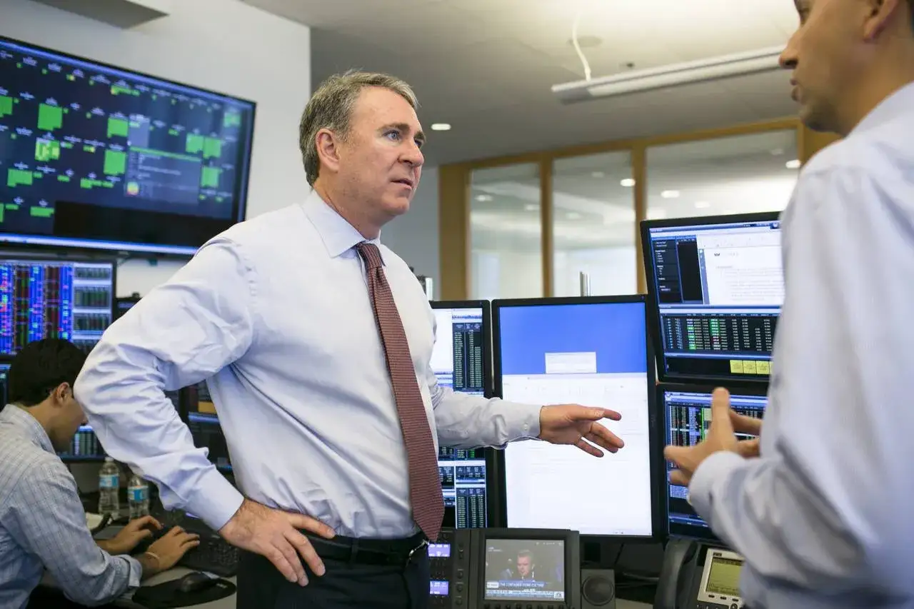 Ken Griffin w biurze, otoczony monitorami z danymi giełdowymi, rozmawia z kolegą.