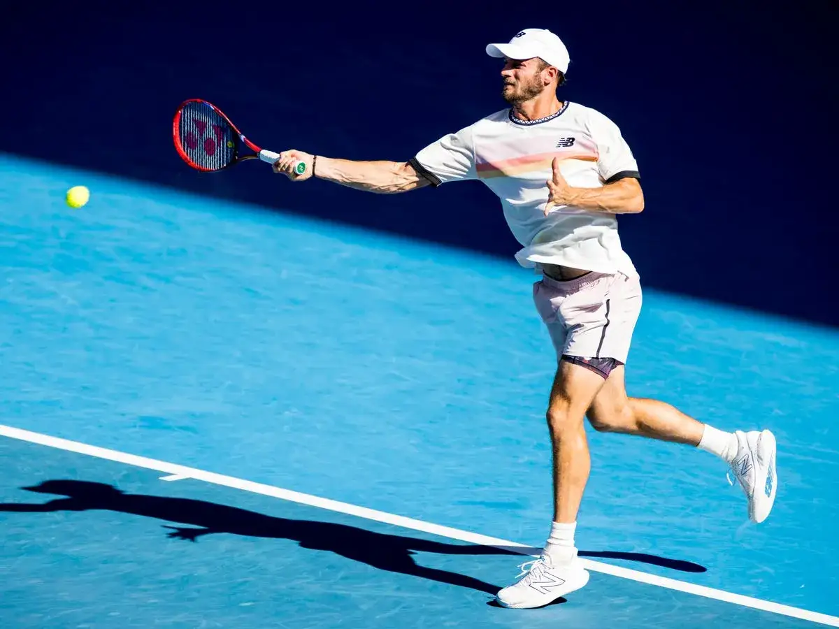 Gracz w **tenis** uderza piłkę na niebieskim korcie.