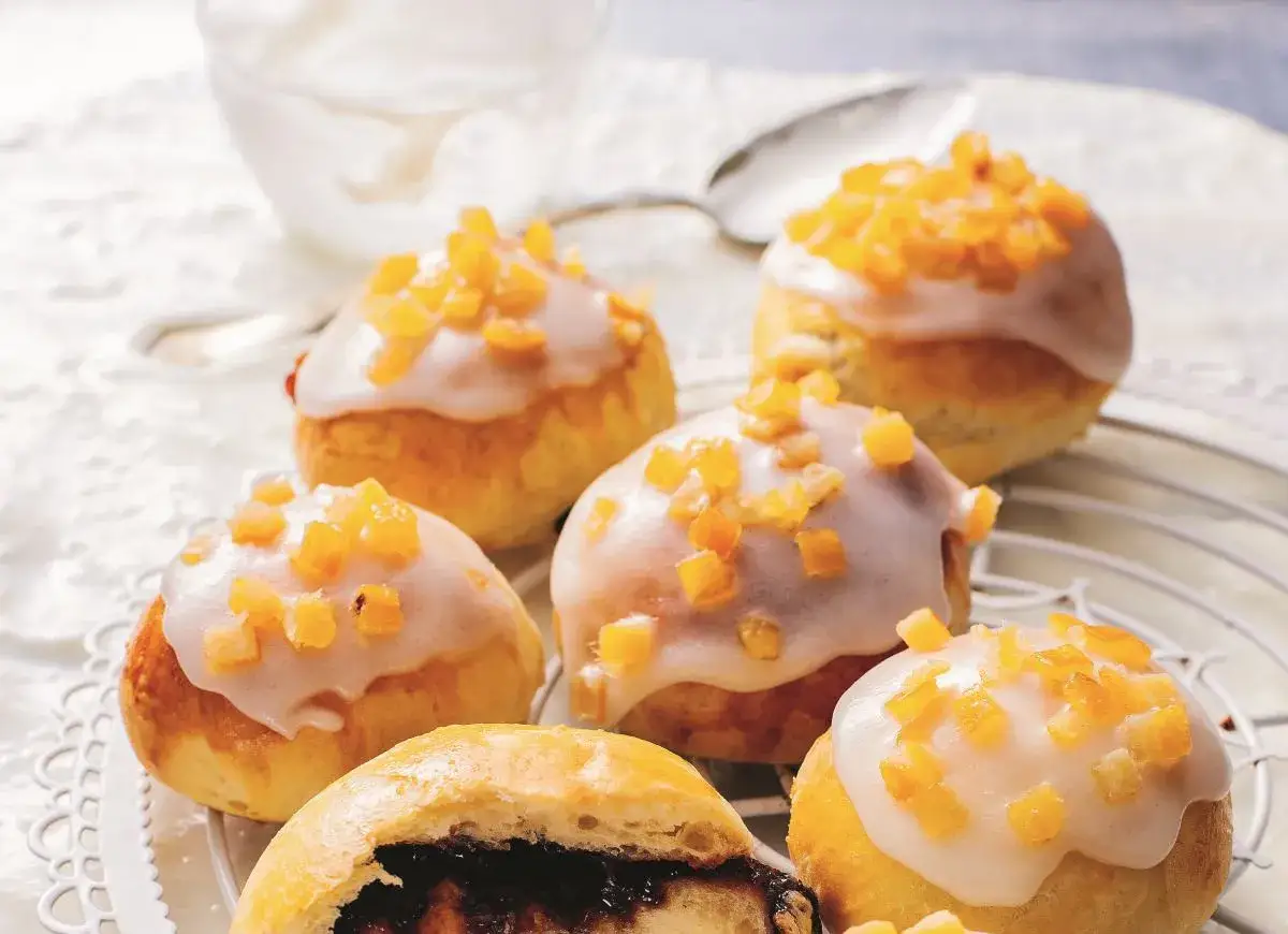 Pyszne, pieczone paczki z lukrem i kandyzowaną skórką pomarańczową. Jeden paczek przekrojony ukazuje ciemne, czekoladowe nadzienie.