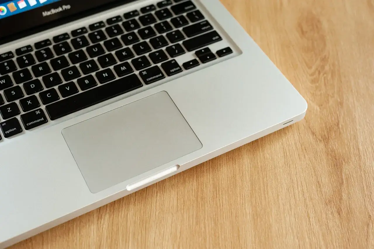 Klawiatura i touchpad MacBook Pro na drewnianym blacie. Dowiedz się, jak włączyć touchpad.