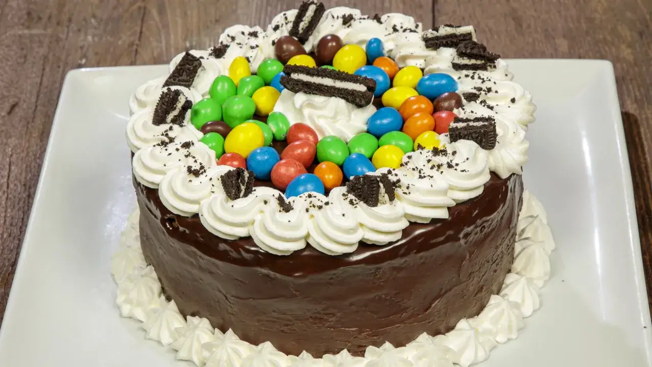 Torta di buon compleanno al cioccolato, decorata con panna montata, caramelle colorate e biscotti Oreo.