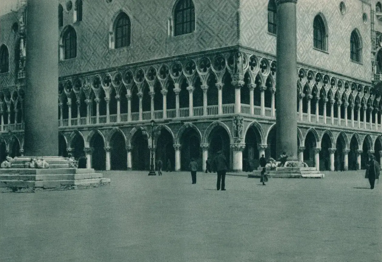 L'entrée du Palais des Doges, avec ses arcades gothiques et ses colonnes imposantes, se dresse majestueusement sur la place. Quelques passants profitent de ce lieu historique.