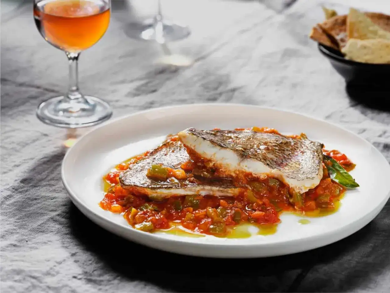 Deliciosa urta a la roteña servida en plato blanco, con guarnición de pimientos y tomate. Copa de vino al lado.