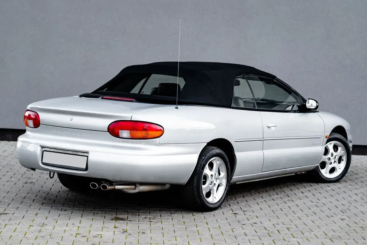 Srebrny kabriolet Chrysler Stratus Limited z czarnym dachem, zaparkowany na kostce brukowej.