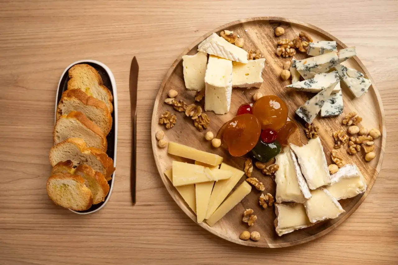 Assortimento di formaggi francesi, noci, frutta candita e crostini su un tagliere di legno.