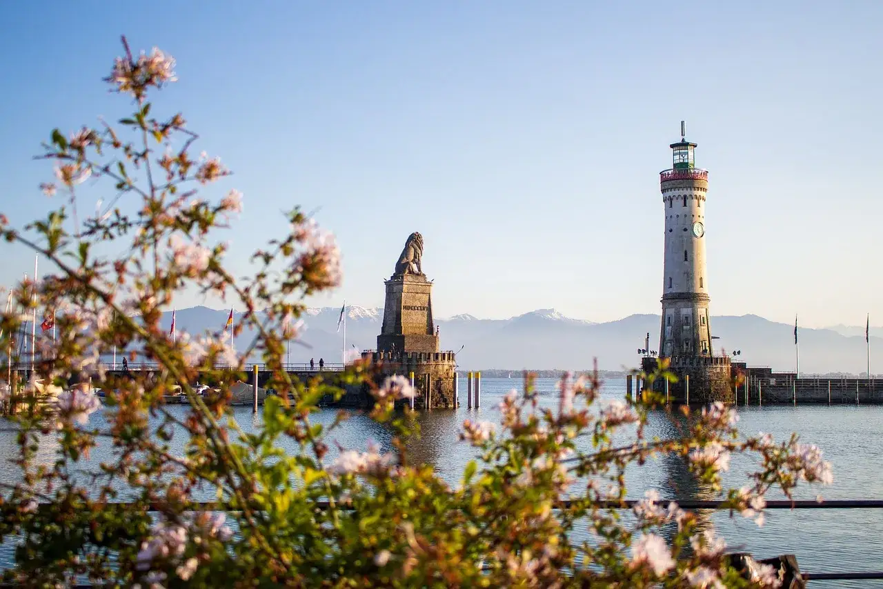 Bl&uuml;hende Zweige im Vordergrund, im Hintergrund der imposante Leuchtturm Lindau und die L&ouml;wenstatue am Hafen.
