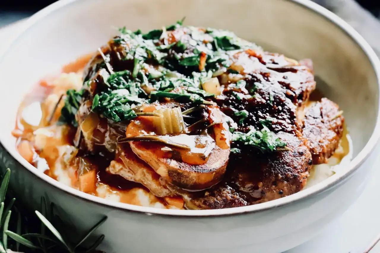 Herzhaftes Ossobuco mit cremiger Polenta als Beilage, garniert mit frischen Kräutern.