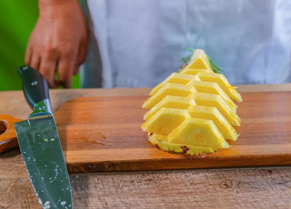 Pokrojony ananas na desce, obok nóż. Proste wskazówki, jak pokroić ananasa, by cieszyć się jego smakiem.