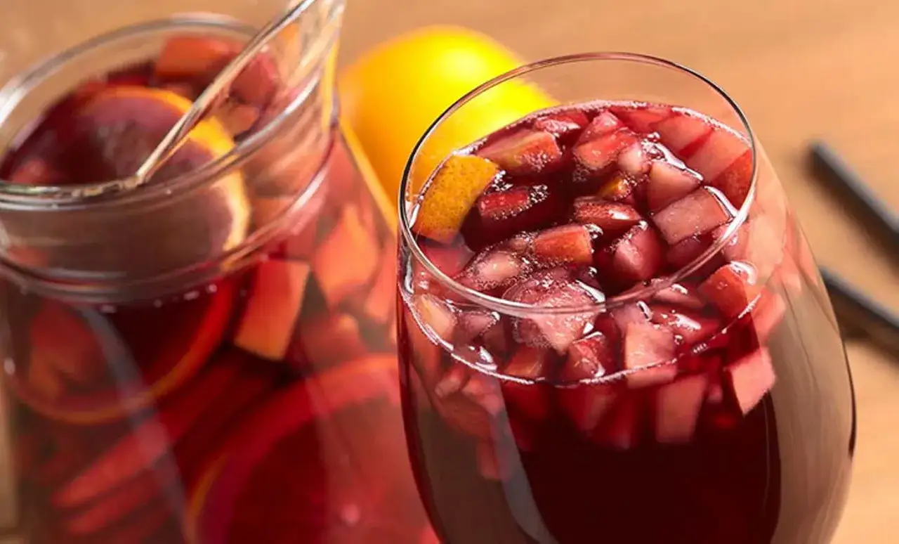 Kusząca Sangria czerwona w szklance i dzbanku, pełna owoców. Czy wolisz ją od Sangrii białej?