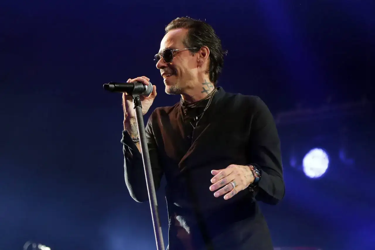 Marc Anthony w okularach przeciwsłonecznych śpiewa do mikrofonu na koncercie.
