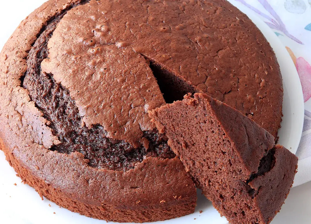 Una soffice torta all'acqua al cacao, con una fetta tagliata che mostra la sua morbidezza.