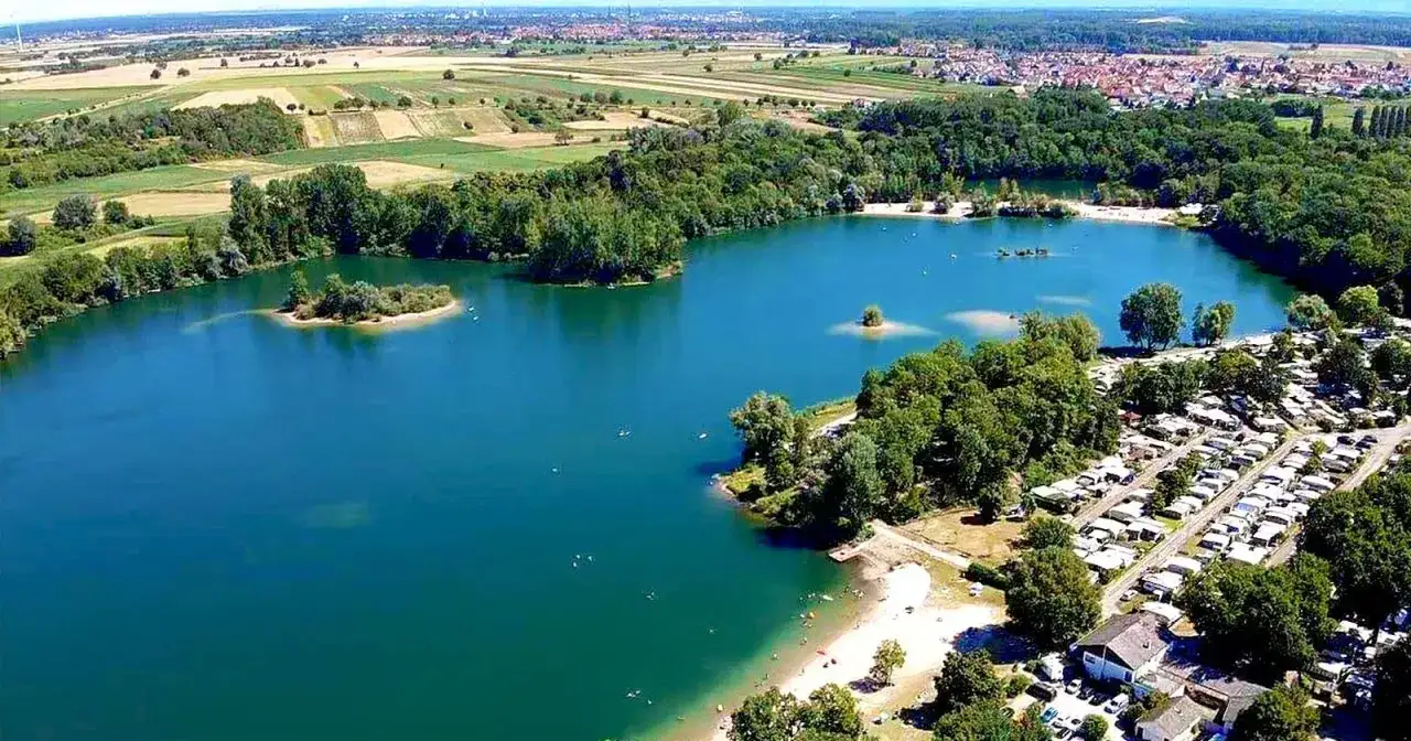 Der Mechtersheim See mit Inseln, Campingplatz und Badegästen.