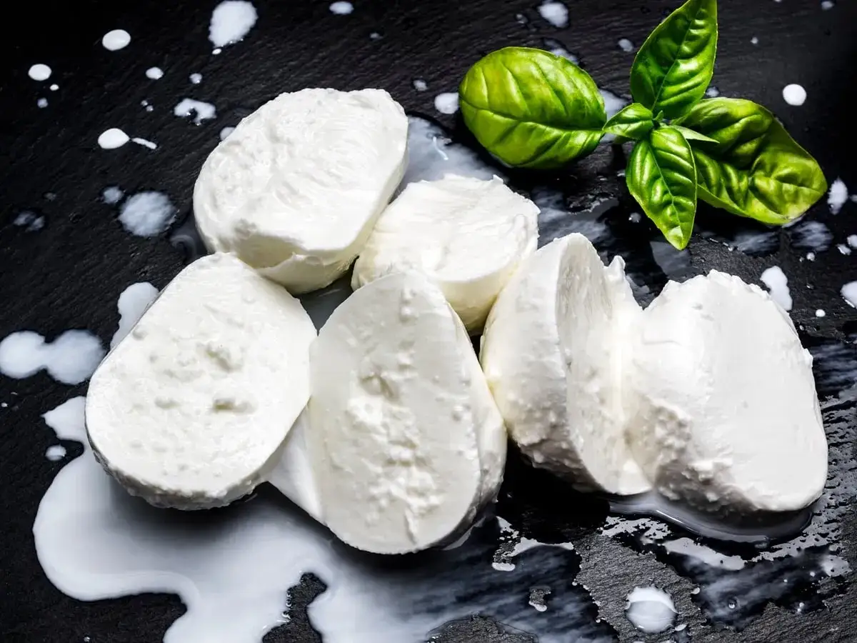 Kuleczki mozzarelli na czarnym tle, obok listki bazylii. Zastanawiasz się nad mozzarella kcal?