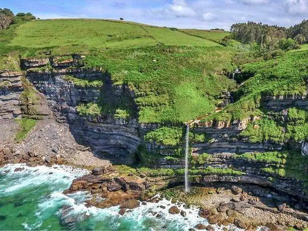 Acantilados verdes con cascada cayendo al mar. Ideal para senderismo en Villaviciosa.