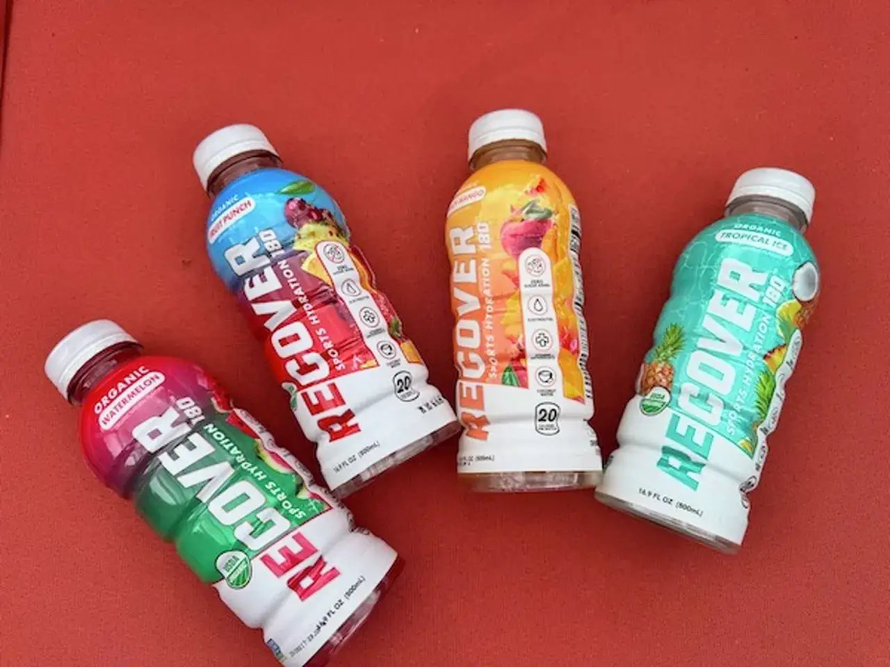 Cztery butelki napoju izotonicznego Recover o różnych smakach: arbuz, punch, mango i tropikalny.