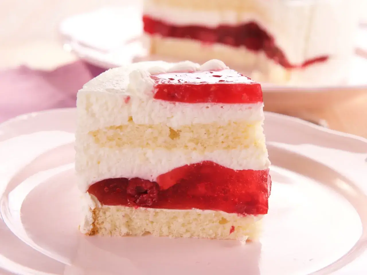 Ein saftiges Stück Frau Holle Kuchen mit Biskuit, Sahne und roter Fruchtfüllung, garniert mit einem Hauch von Sahne.