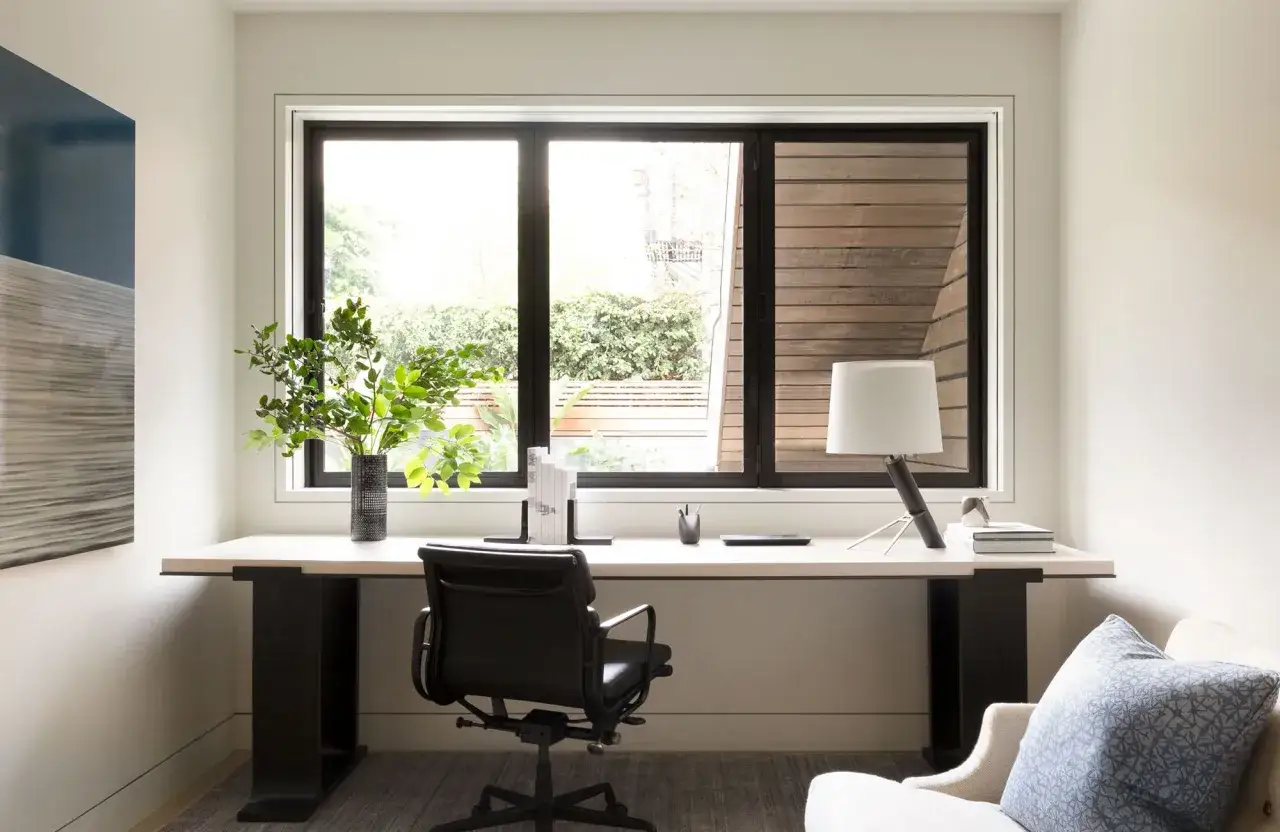 Ein modernes Homeoffice mit Schreibtisch, B&uuml;rostuhl und gro&szlig;em Fenster, das viel Tageslicht hereinl&auml;sst.