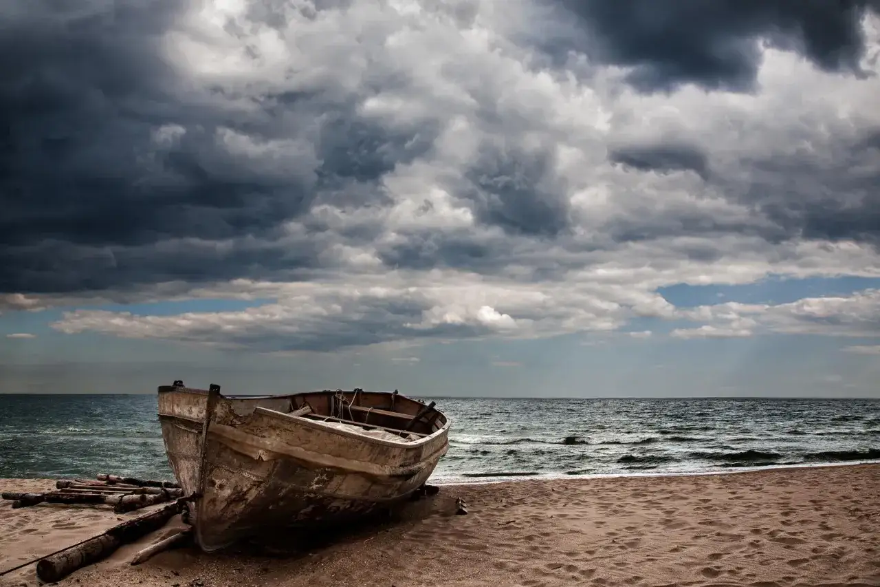 Stara łódź na plaży, burzowe chmury nad morzem. Jak w