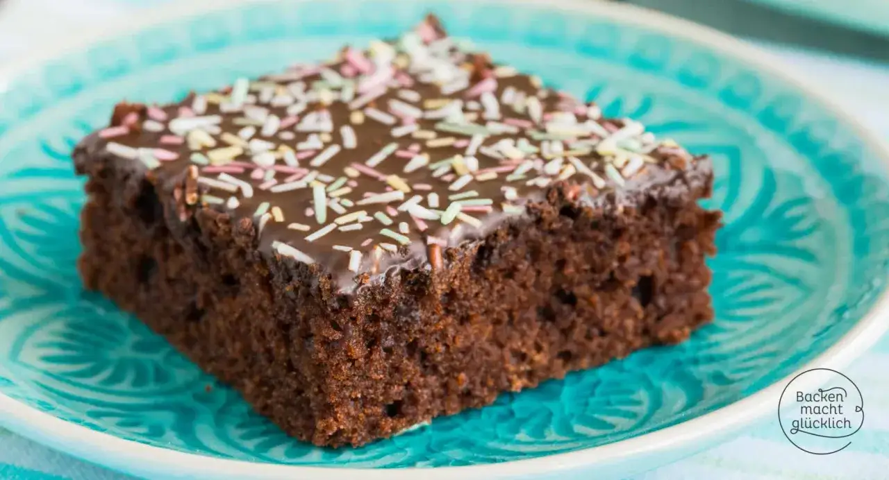 Ein Stück saftiger Schokokuchen vom Blech, mit Schokoladenglasur und bunten Streuseln, auf einem türkisfarbenen Teller.