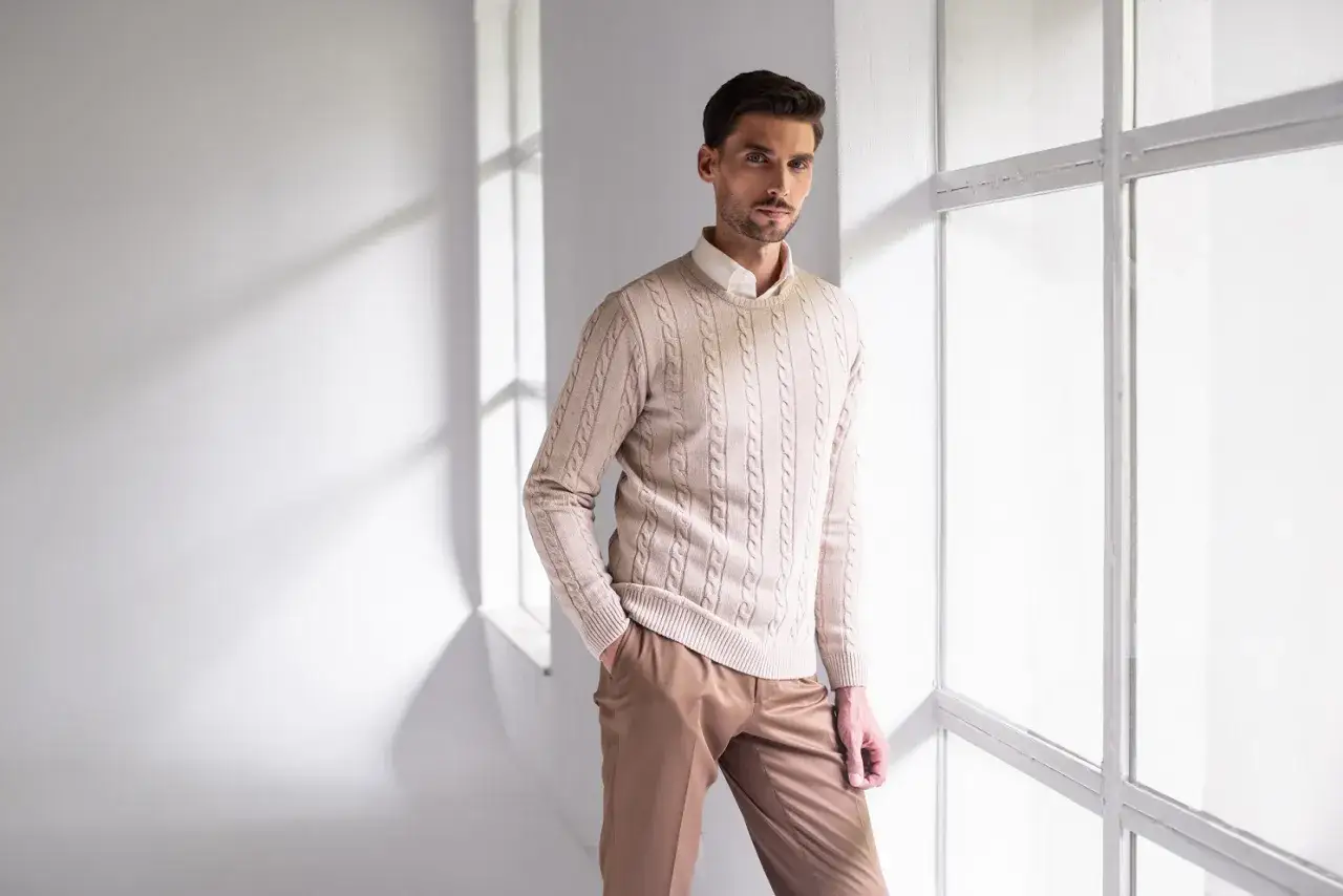 Elegancki beżowy sweter z warkoczami i brązowe spodnie to idealna stylizacja, co ubrać na sylwestra na domówkę.