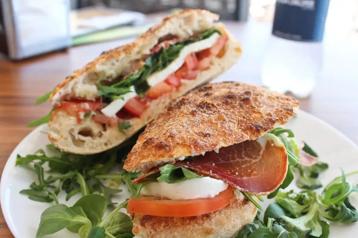 Due paposcia freschi, uno con prosciutto crudo, mozzarella e pomodoro, l'altro con pomodoro e mozzarella, serviti su un letto di rucola. Un assaggio di Peschici.