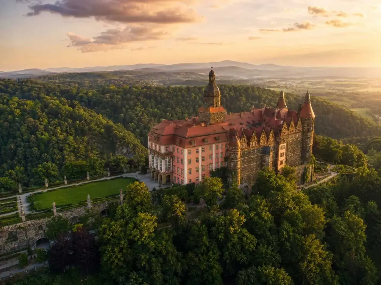 Zamek Książ, jedna z największych atrakcji w okolicach Wrocławia, w otoczeniu zielonych wzgórz o zachodzie słońca.