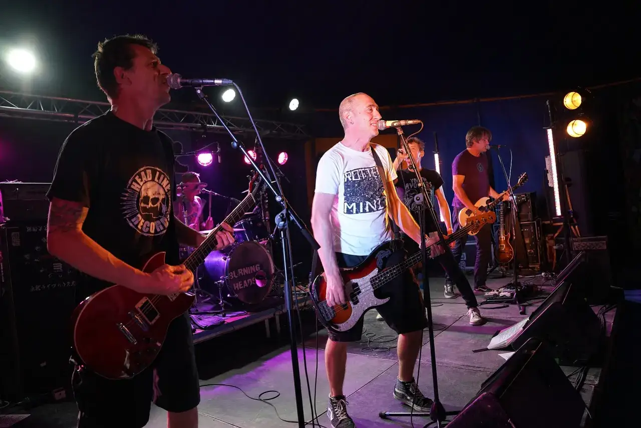 Le groupe Burning Heads en pleine action sur scène, guitares électriques et basse résonnent sous les lumières.