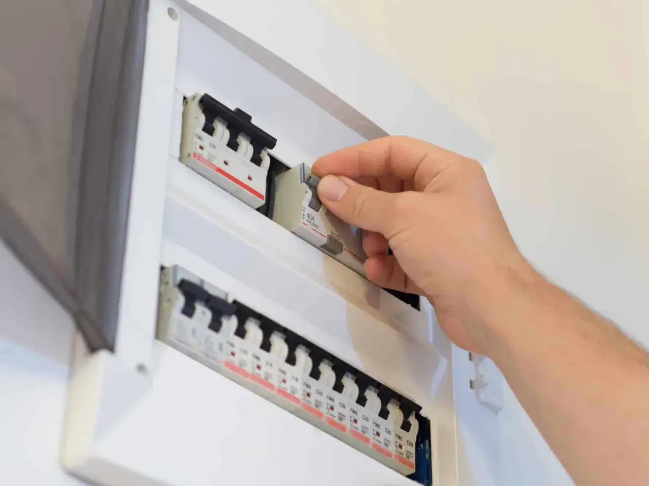 Main d'un &eacute;lectricien manipulant un disjoncteur d'abonn&eacute; dans un tableau &eacute;lectrique.