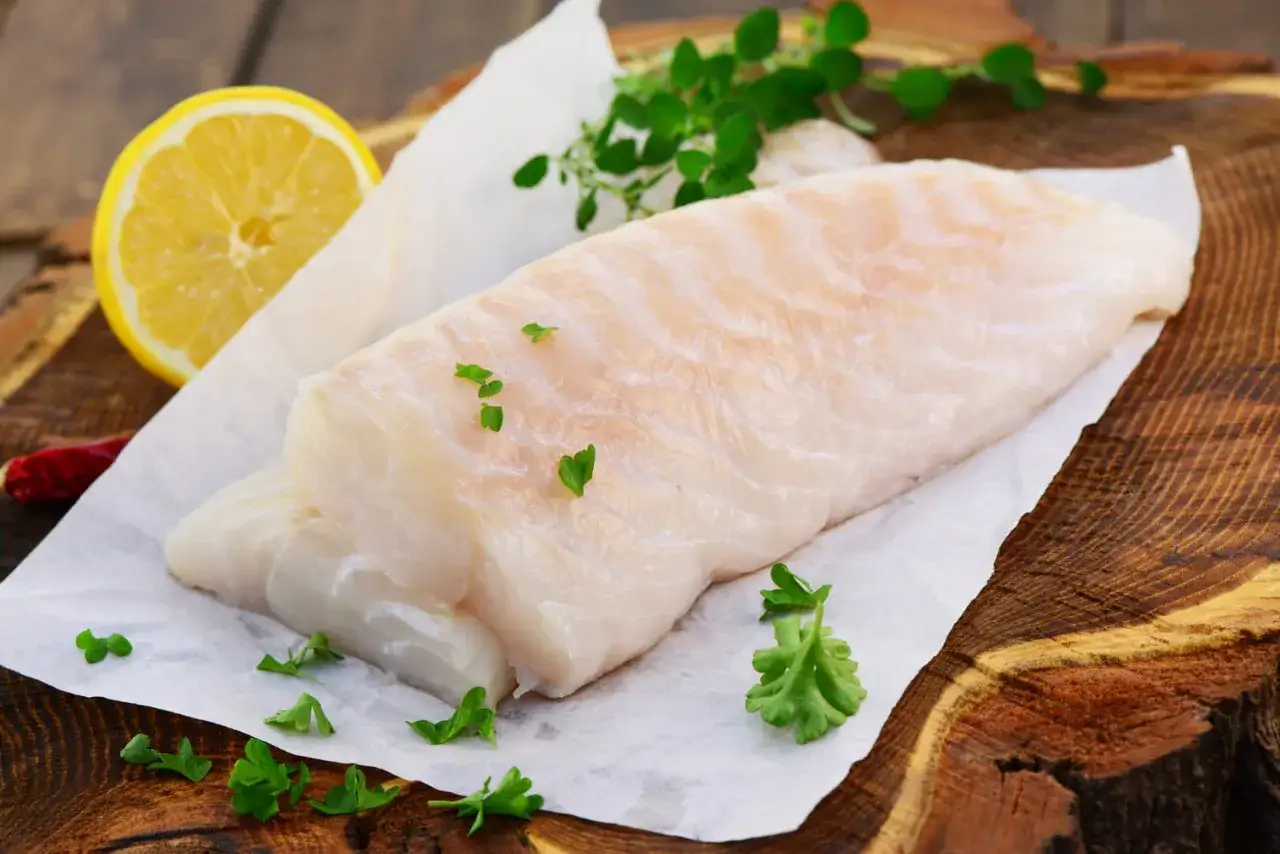Deux beaux filets de cabillaud poisson, prêts à être cuisinés, avec du citron, des herbes et un piment sur une planche en bois.