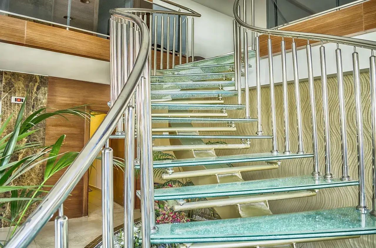 Nowoczesne schody wachlarzowe ze szklanymi stopniami i metalową balustradą, tworzące elegancką spiralę.