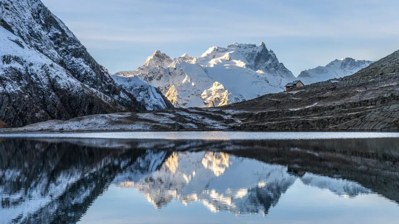 Reflets d'un lac paisible près de Briançon, avec des montagnes enneigées et un refuge. Une parfaite image pour une randonnée.