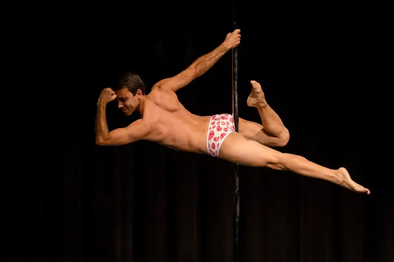 Mężczyzna w białych slipach z ustami wykonuje dynamiczny ruch podczas występu pole dance.