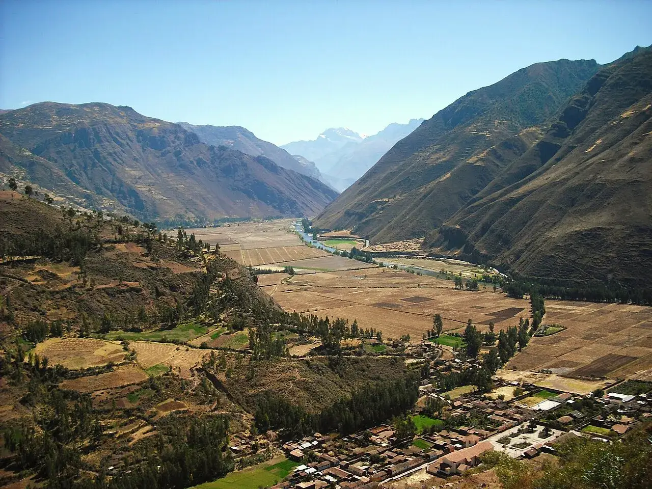 Weites Tal mit Fluss und Feldern im **heiligen Tal Peru**. Berge und ein Dorf s&auml;umen die Landschaft.