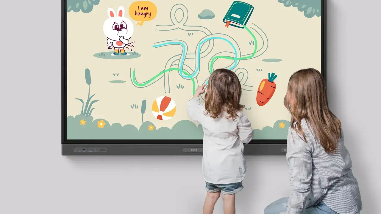 Bambini interagiscono con un gioco didattico multimediale su un grande schermo, aiutando un coniglietto affamato a raggiungere una carota.