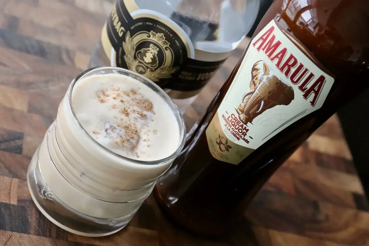 En krämig Amarula drink, toppad med kanel, bredvid flaskan.