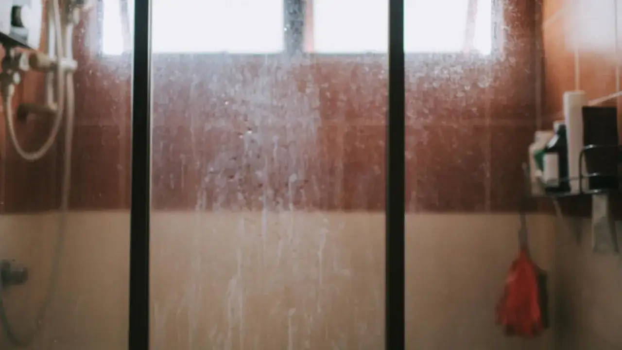 Mampara de ducha con marcas de agua y jab&oacute;n, lista para la limpieza.
